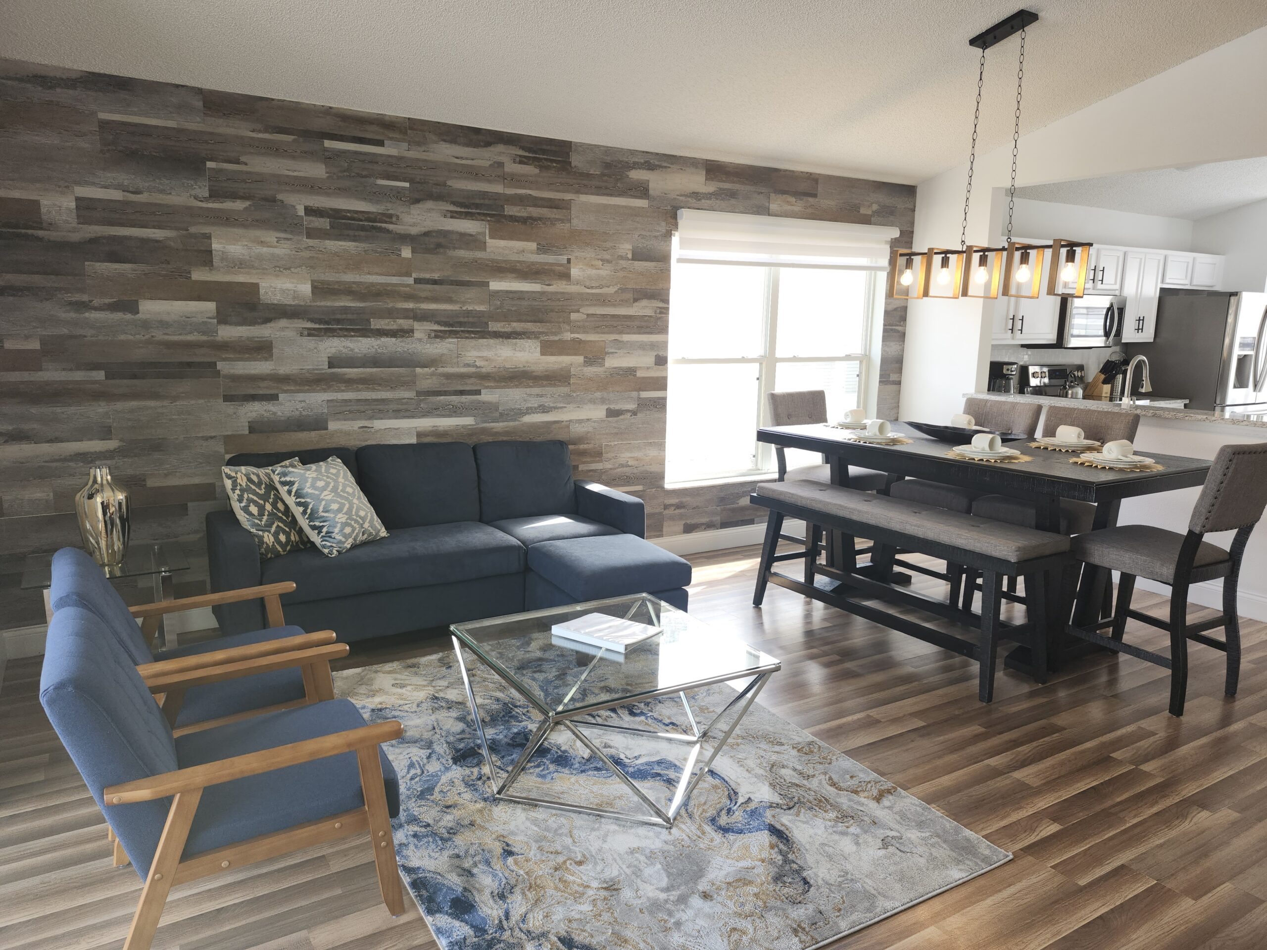 Open-concept Airbnb living and dining room design in Orlando with wood-look accent wall and industrial lighting