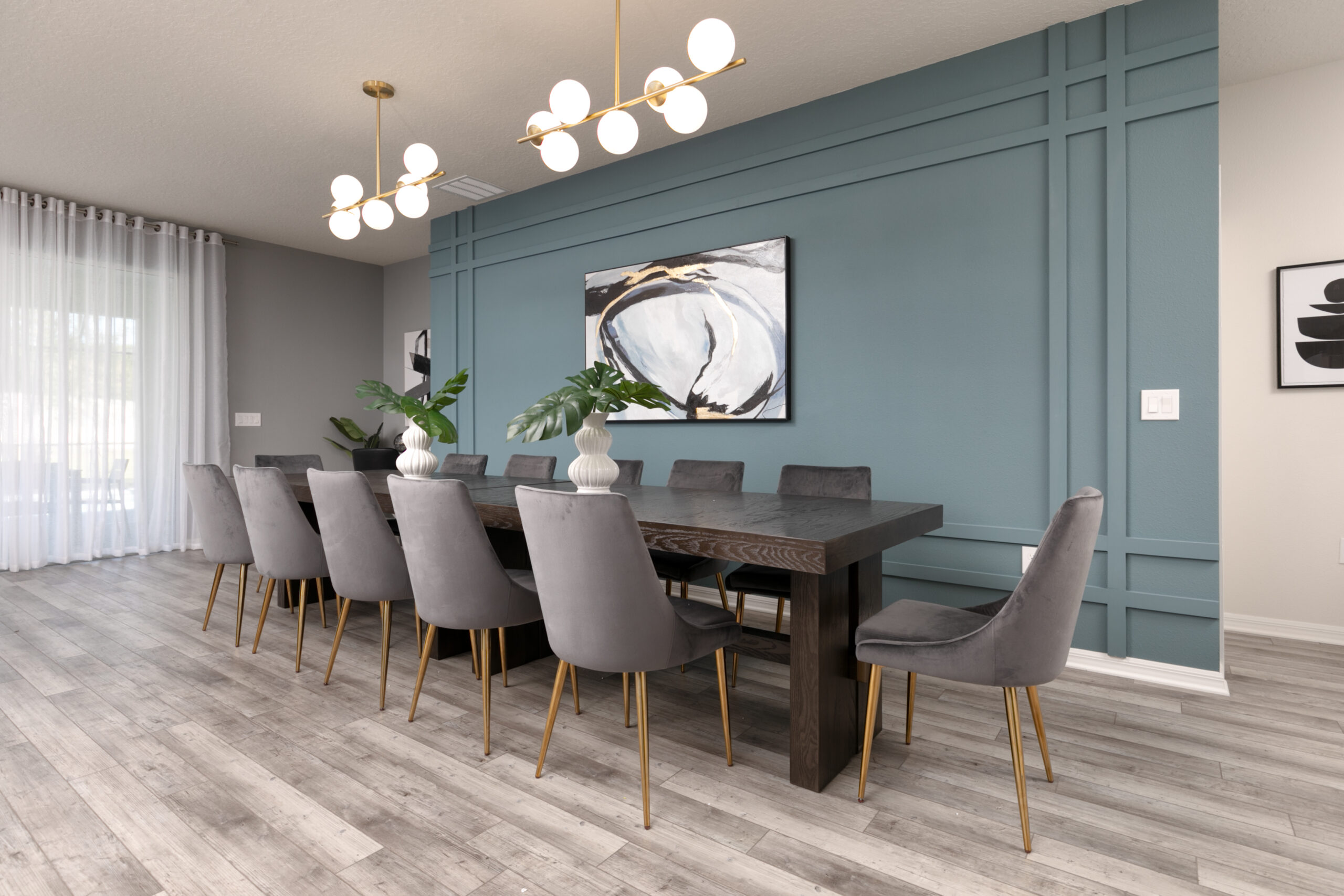 Elevated Airbnb dining room design in Orlando with teal accent wall, brass chandeliers and long dining table