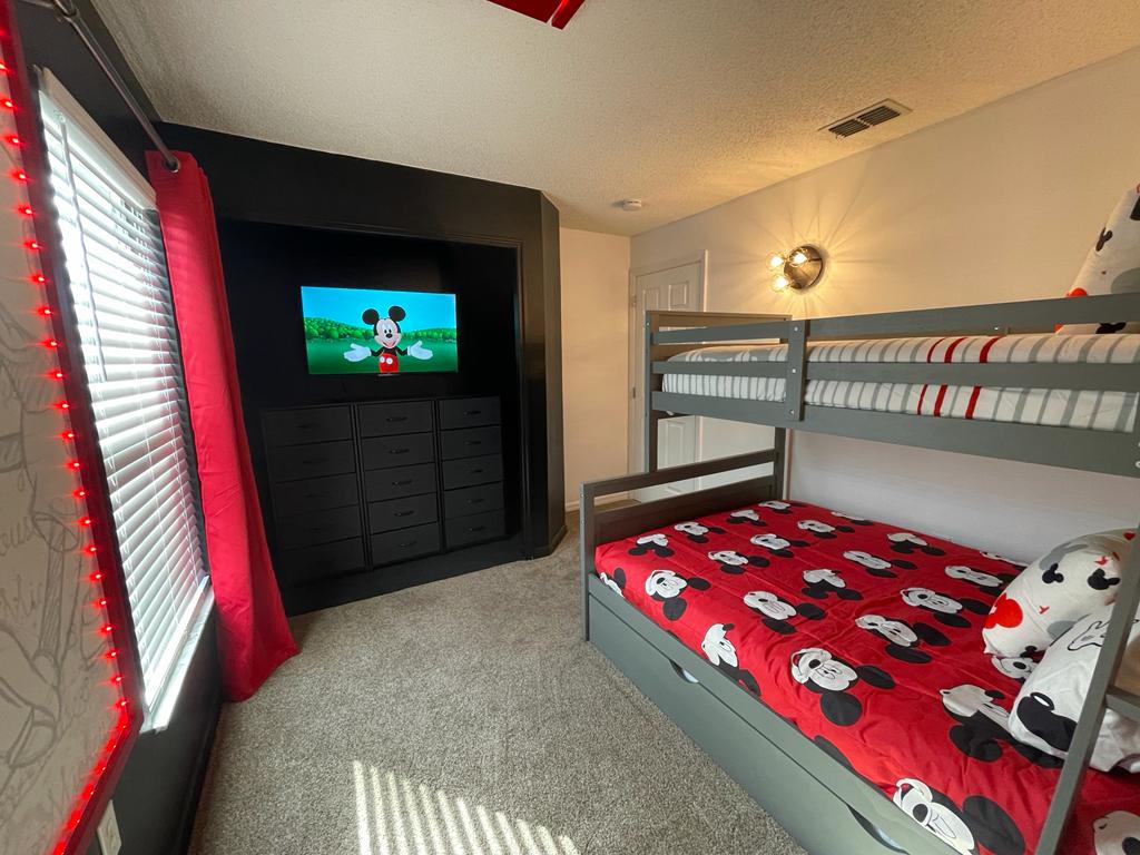 Classic Mickey Mouse themed bunk bedroom in an Orlando vacation rental with red accent wall and TV playing Mickey Mouse Clubhouse